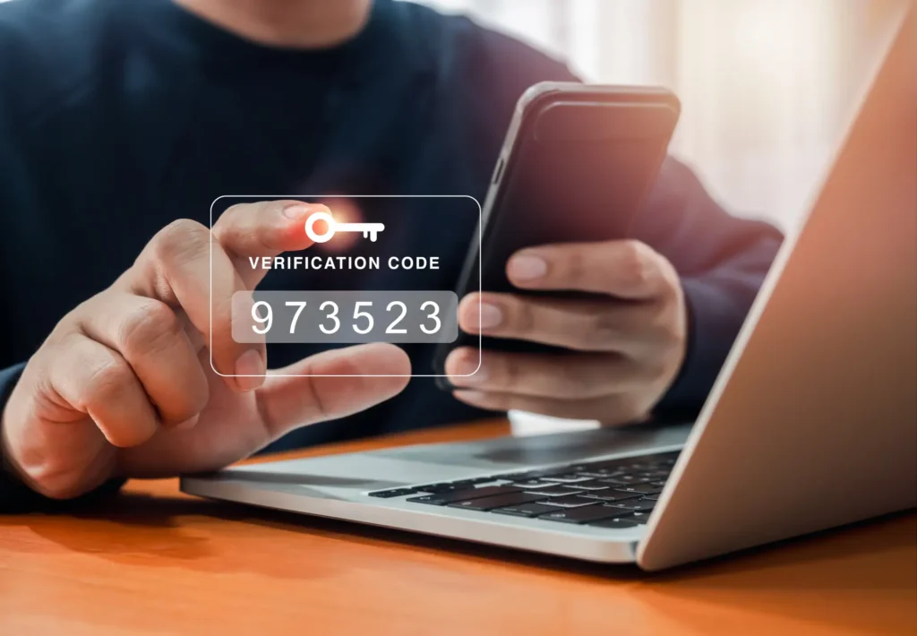 Osoba trzymająca smartfon i dotykająca wirtualny ekran z kodem weryfikacyjnym i ikoną klucza, symbolizujący dwufaktorowe uwierzytelnianie.